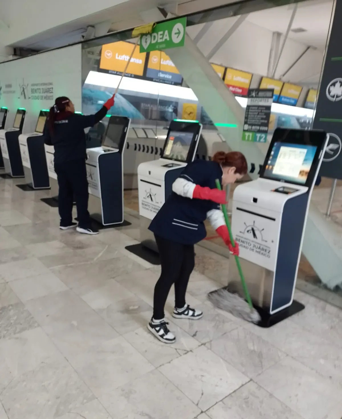 Dos integrantes de Grupo Lyon limpiando los módulos de autoregistro del aeropuerto