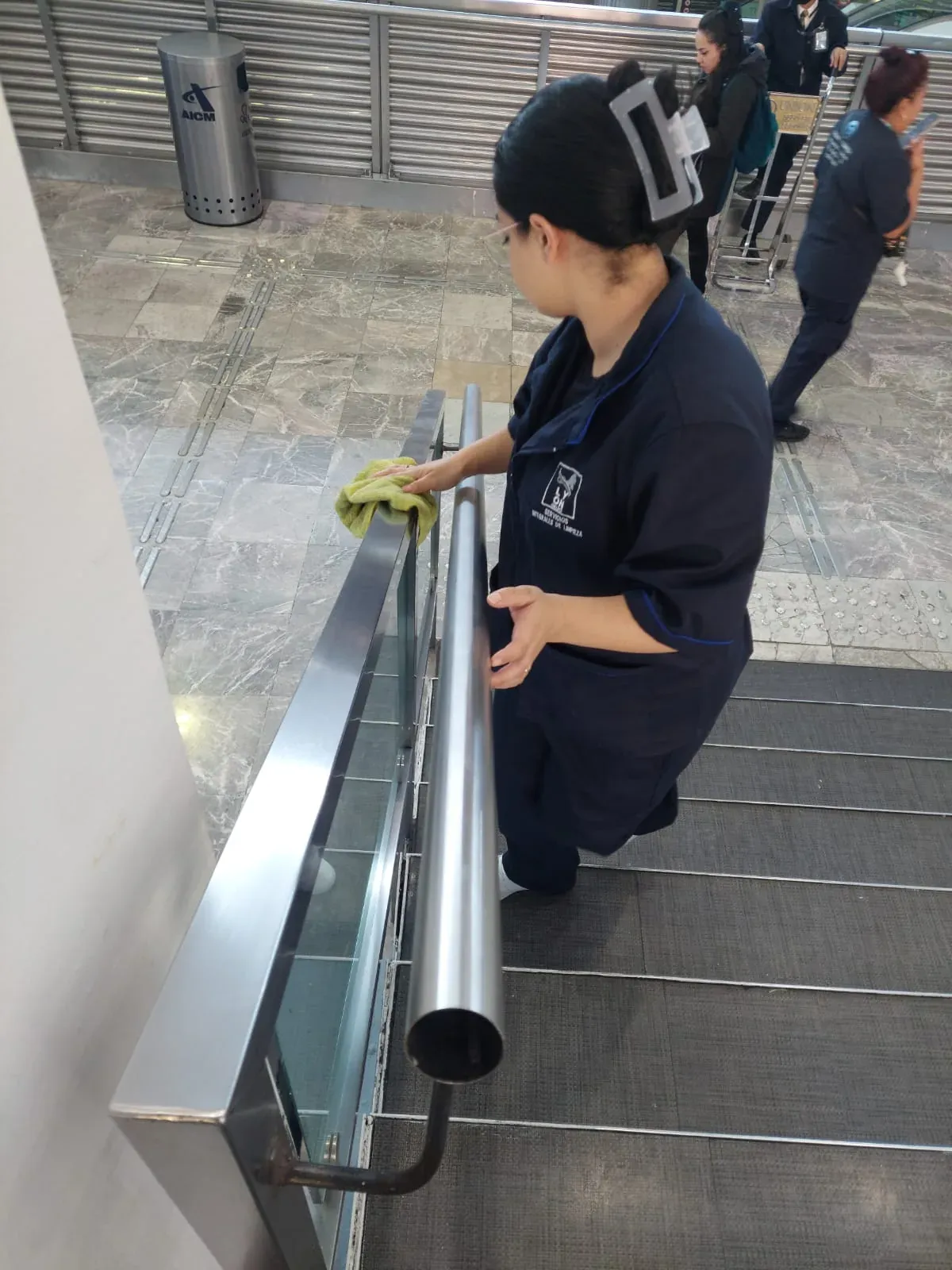 Integrante de Grupo Lyon limpiando el pasamanos de una escalera eléctrica del aeropuerto