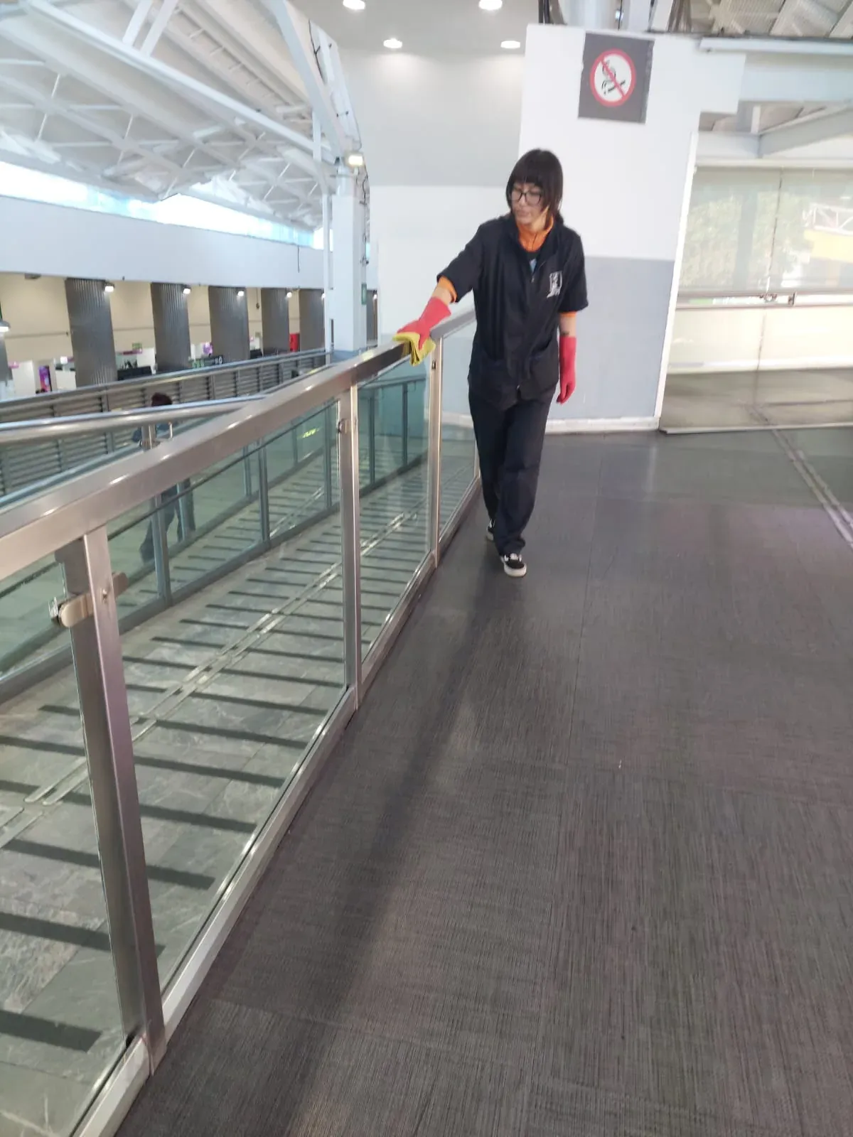 Integrante de Grupo Lyon con guantes limpiando el barandal de la pasarela del aeropuerto