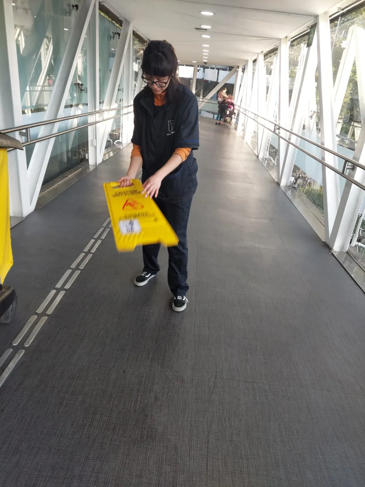 Integrante de Grupo Lyon colocando un señalamiento de piso mojado en la pasarela del aeropuerto