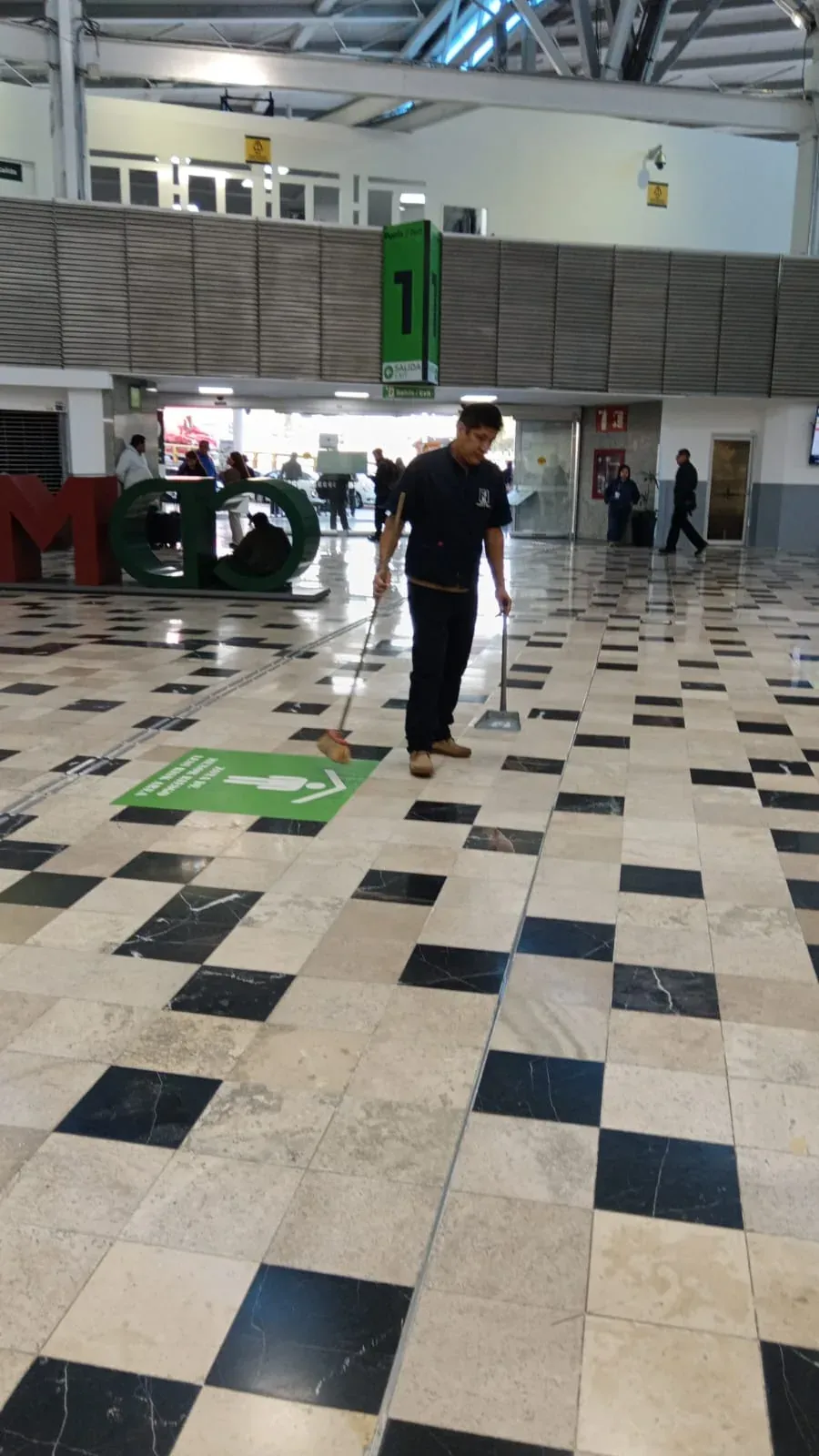 Personal de Grupo Lyon barriendo junto al letrero de la Puerta 1 del aeropuerto