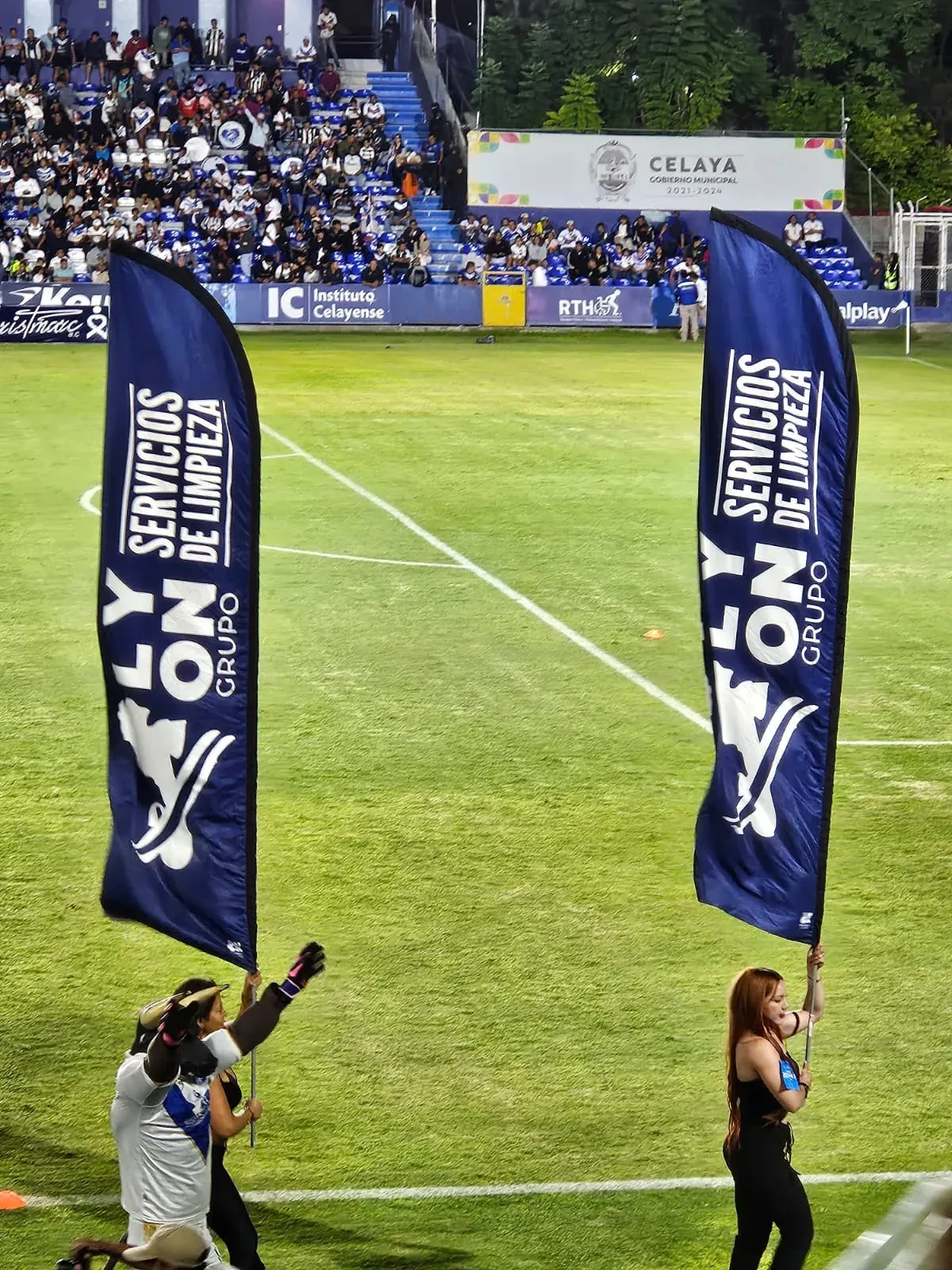 Banderas de Grupo Lyon Servicios de Limpieza sostenidas en la cancha de un estadio